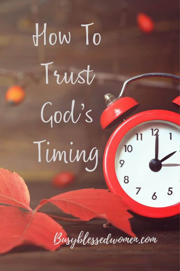 how to trust God's timing- old fashioned red alarm clock with 2 bells on top sitting on wood table with red leaves 