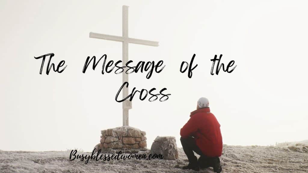 The message of the cross- man in red winter jacket and grey stocking cap half kneeling on frozen ground before a plain wooden cross on a rock base.