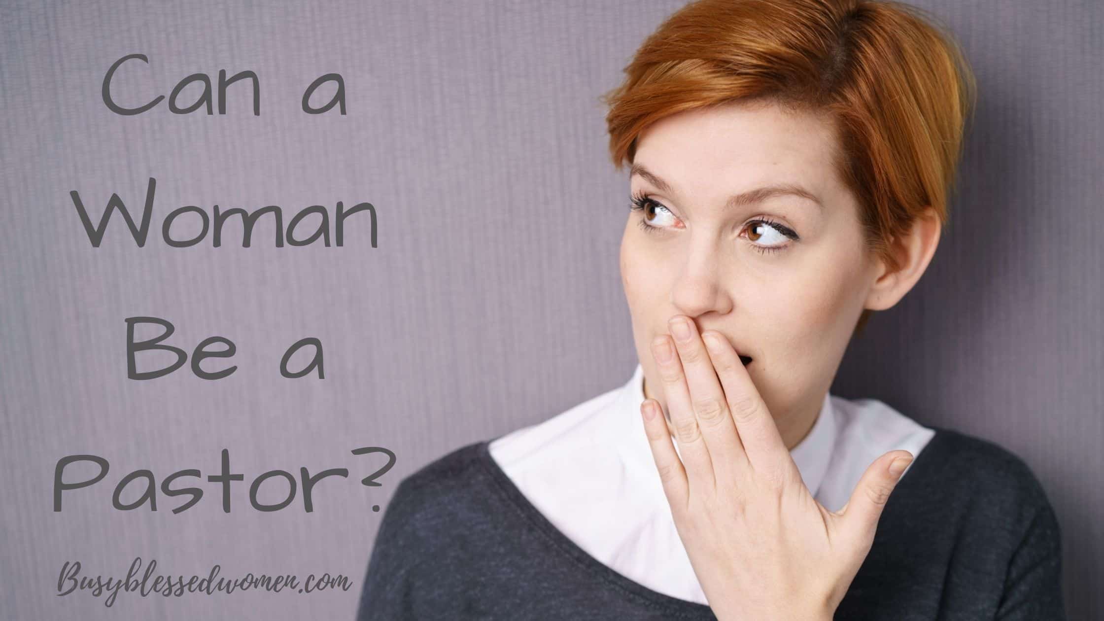 Woman with short red hair dressed in dark sweater and white blouse with hand over her mouth