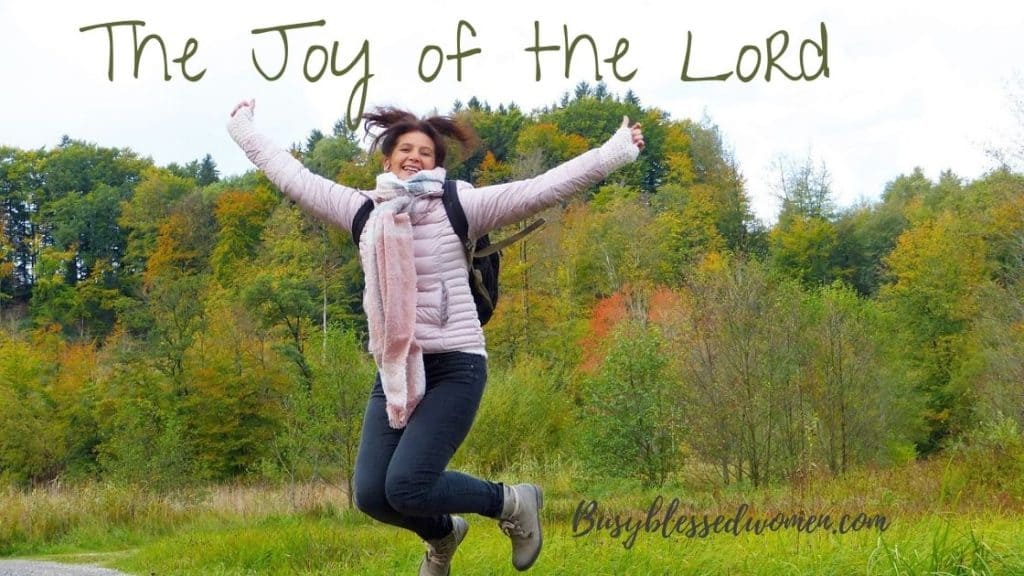 The Joy of the Lord- woman in white winter coat, jeans, boots, backpack jumping with arms outstretched in fall forest area