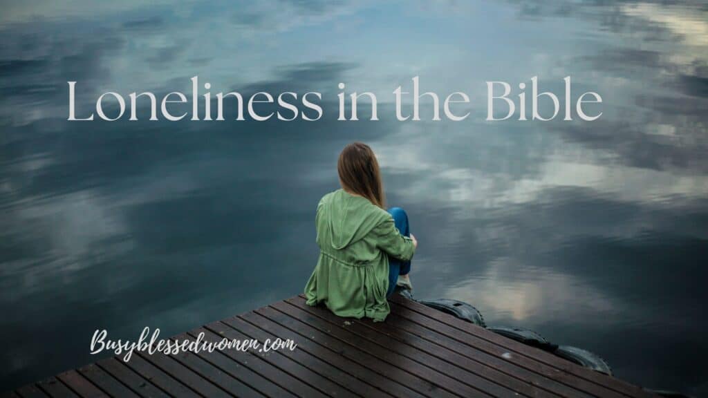 loneliness in the Bible- woman in green jacket and jeans sitting on a dark wooden dock with knees drawn up to her chest, looking out over the water