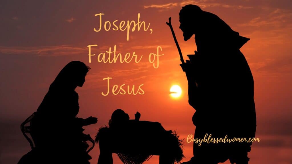 dark silhouette of Joseph  standing near manger with walking stick, Mary kneeling, and Jesus' head visible against a deep orange sunset sky.