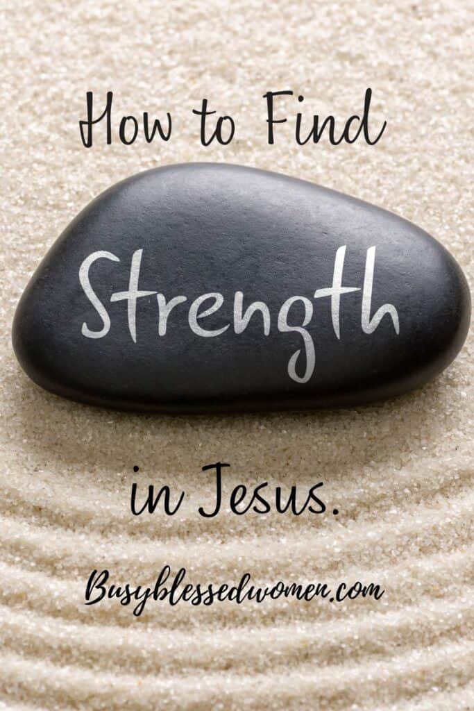 Jesus is our strength- smooth black rock with the word "strength" written on it with white ink, lying on sand