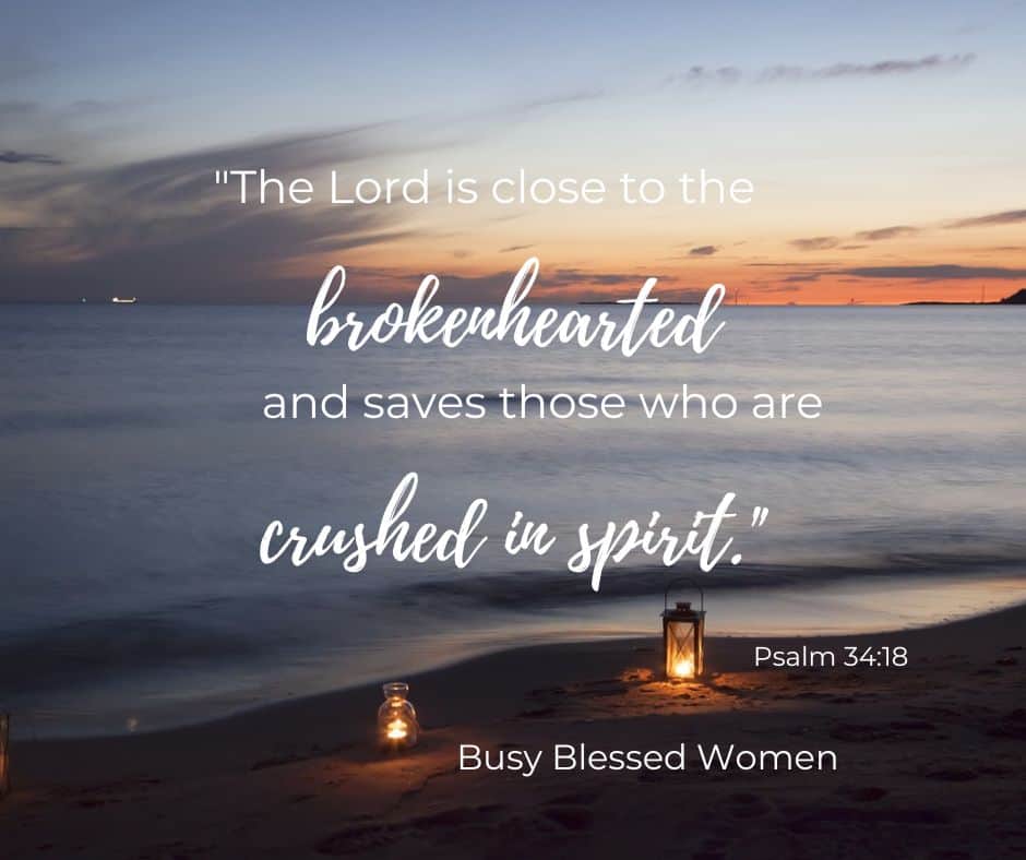 Psalm 34:18 verse overlay on photo of lake at sunset with lanterns on beach